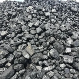 Góra czarnego węgla kamiennego o nieregularnych kształtach, z widocznymi refleksami światła na powierzchni brył.