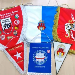 Kolekcja ozdobnych proporczyków i chorągiewek z frędzlami, prezentujących herby, logotypy i napisy związane z klubami sportowymi, organizacjami i miastem Kraków, w tym proporczyk Wisły Kraków...