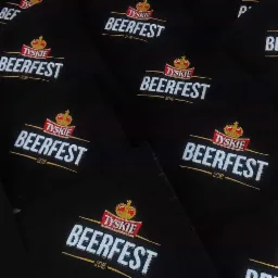 Czarne koszulki z wyhaftowanym logo 'Tyskie Beerfest 2016', ułożone pod kątem, widoczne detale haftu i tekstura materiału.