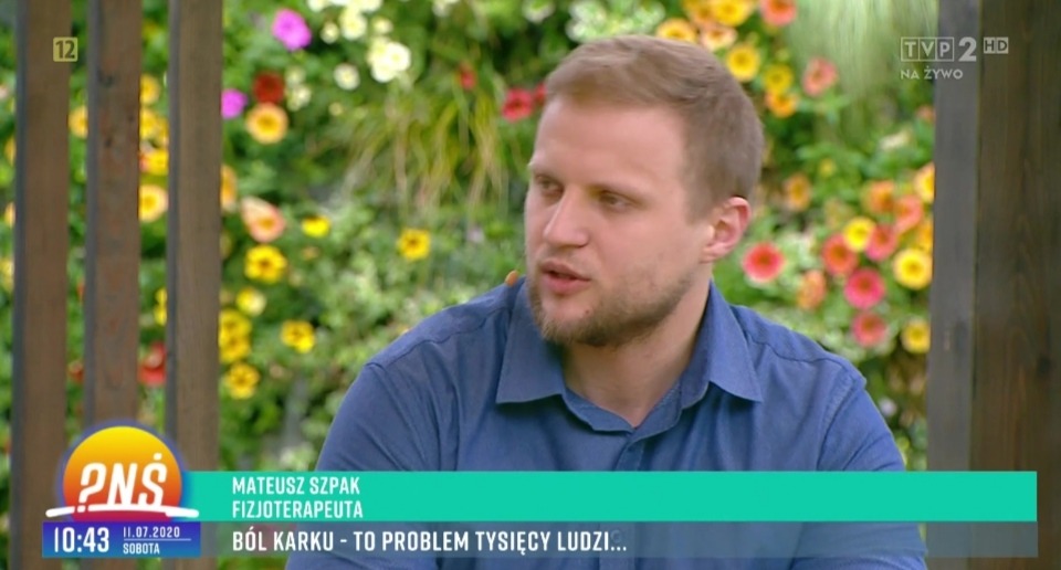 Portret fizjoterapeuty Mateusza Szpaka podczas wywiadu telewizyjnego na tle kwiatów, omawiającego problem bólu karku.