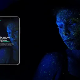 Ekran smartfona wyświetla twarz kobiety pokrytą fluorescencyjnymi plamkami w odcieniach niebieskiego i zielonego, z hasłem 'The best way to predict the future is to invent it' na czarnym tle, obok...