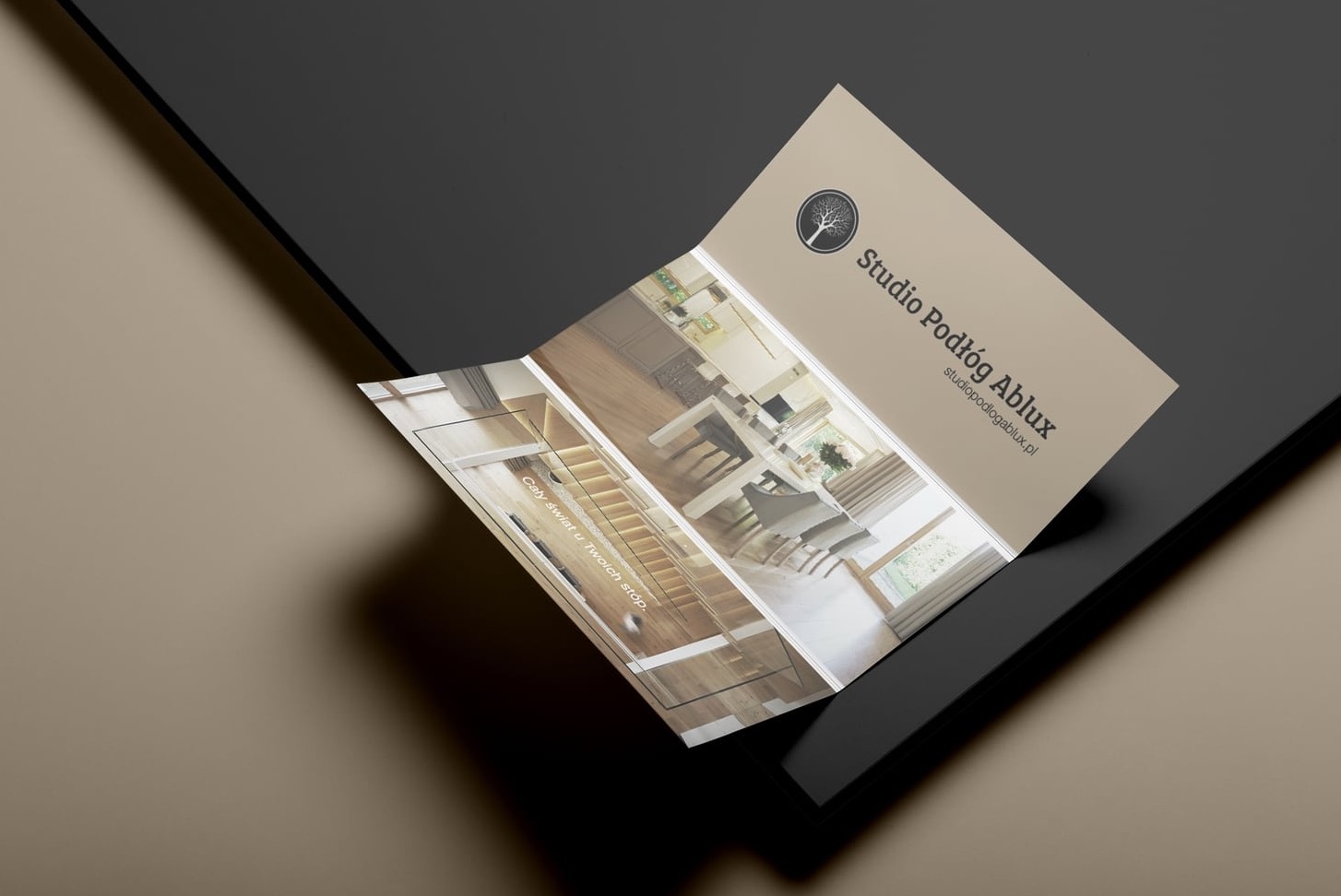 Rozłożona ulotka reklamowa Studio Podłóg Ablux prezentująca aranżacje wnętrz z drewnianymi podłogami i schodami, leżąca na dwukolorowym tle.