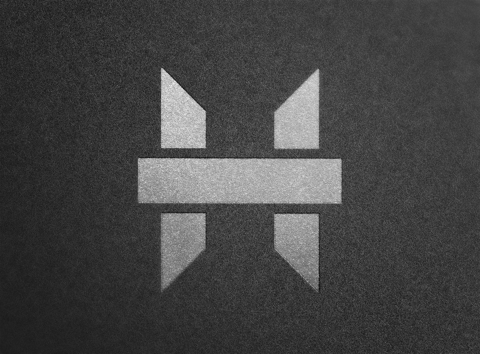 Abstrakcyjne srebrne logo na ciemnoszarym, teksturowanym tle, składające się z geometrycznych kształtów: prostokąta i dwóch par trójkątów.