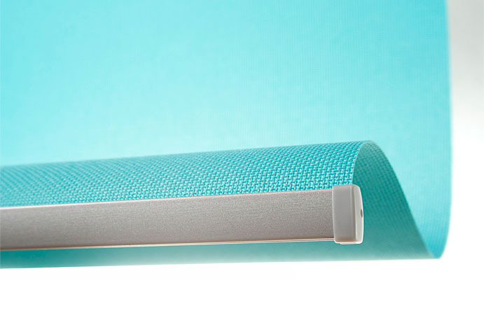 Turkusowa roleta okienna z widoczną fakturą materiału i srebrną listwą montażową, zwinięta w górnej części okna.