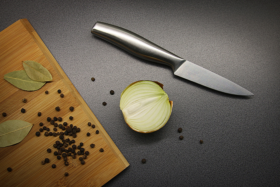 Martwa natura z przekrojoną cebulą, nożem ze srebrną rękojeścią, ziarnami pieprzu i liśćmi laurowymi na desce do krojenia w Poznaniu.