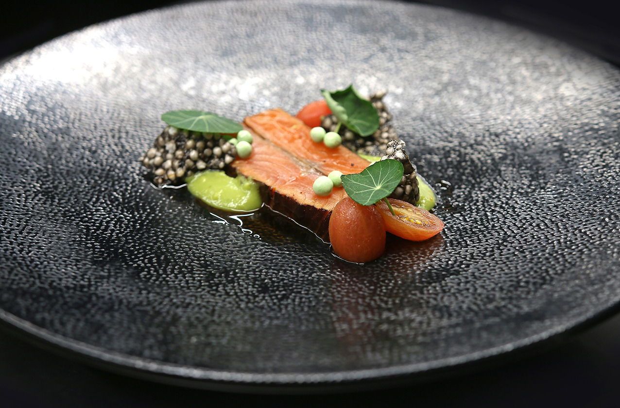 Elegancko podany filet z łososia z zielonymi groszkami, pomidorkami cherry i dekoracyjnymi listkami na talerzu o fakturze przypominającej skórę.