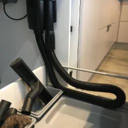 Czarny moduł centralnego odkurzacza z dwiema rurami w szafce, widoczne końcówki i szczotki w szufladzie.