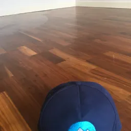 Świeżo umyta, lśniąca drewniana podłoga z widoczną czapką z logo firmy sprzątającej w rogu kadru.