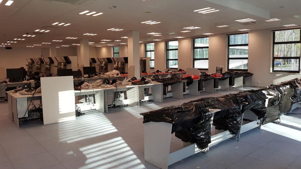 Przestrzeń biurowa z biurkami i komputerami przygotowywana do transportu, część sprzętu zabezpieczona czarną folią