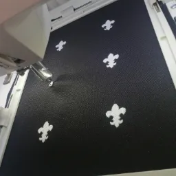 Czarny materiał w tamborku maszyny do szycia z wyhaftowanymi białymi motywami lilii.