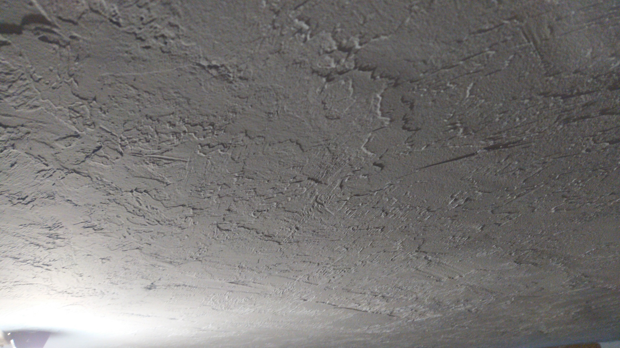Szara, nierówna powierzchnia sufitu z wyraźną fakturą, widoczne ślady po narzędziach, delikatne światło w dolnej części kadru.