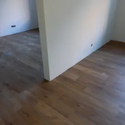 Nowo ułożone panele podłogowe w odcieniach brązu, widok na fragment pomieszczenia z białymi ścianami i wystającymi gniazdkami elektrycznymi.