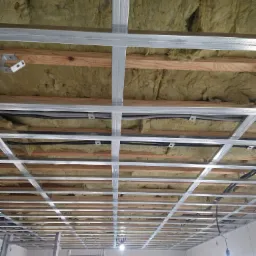 Sufit w trakcie ocieplania wełną mineralną i montażu metalowego stelażu pod płyty gipsowo-kartonowe, widoczne drewniane elementy konstrukcyjne i instalacje elektryczne