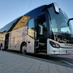 Nowoczesny autokar Setra S 515 HD z otwartymi drzwiami, zaparkowany na chodniku, z odbiciem budynku z zegarem w szybach.