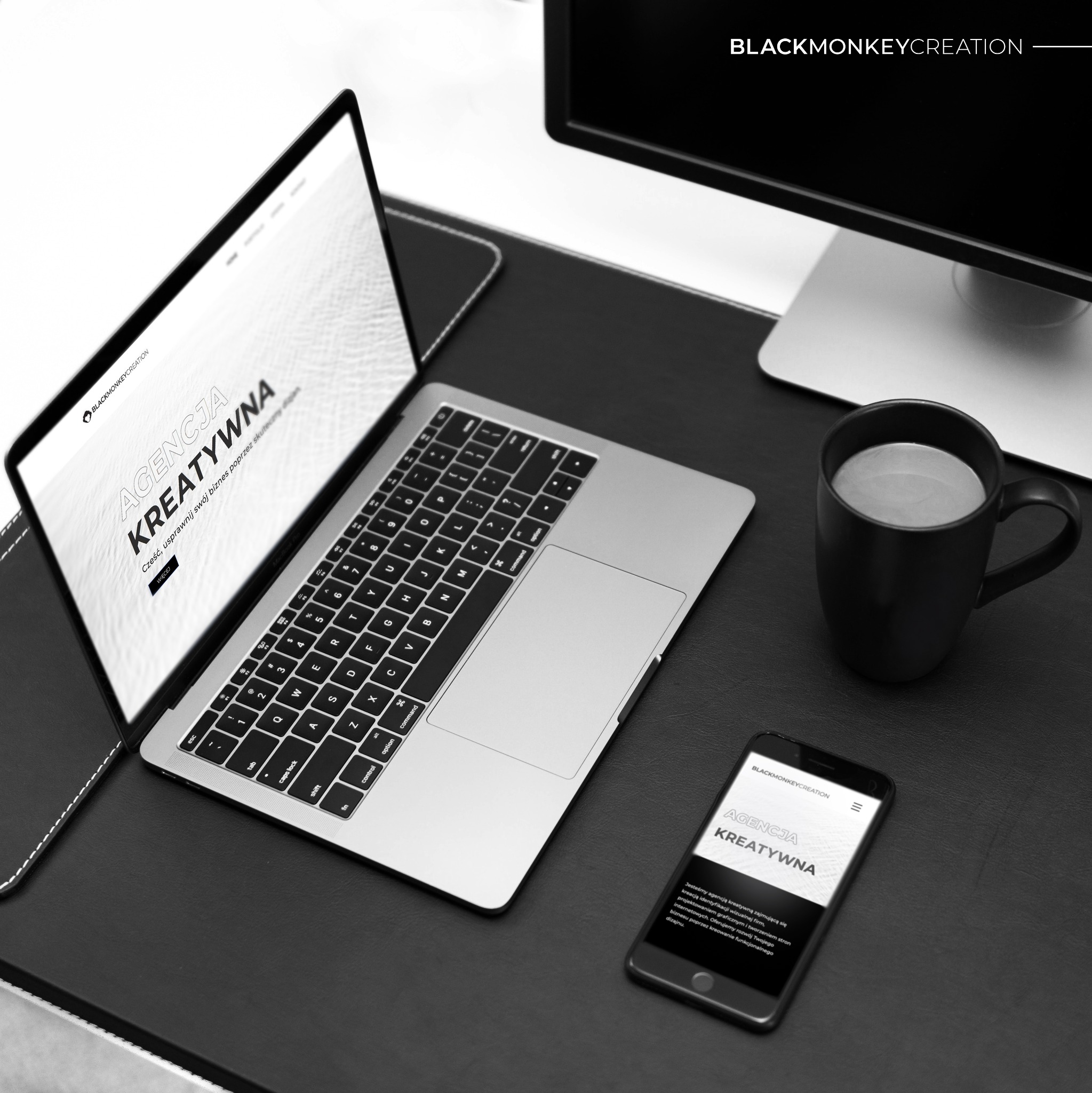 Czarno-białe zdjęcie biurka z laptopem, smartfonem, kubkiem kawy i monitorem. Na ekranie laptopa i smartfona wyświetlona strona internetowa agencji kreatywnej BlackMonkeyCreation.