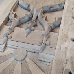 Element drewnianej konstrukcji z rzeźbionymi detalami, widoczne ślady obróbki i przygotowania do dalszej renowacji lub wykończenia.