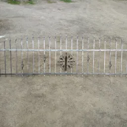 Metalowa, ozdobna brama ogrodzeniowa z kutymi detalami leżąca na szarej, żwirowej nawierzchni.