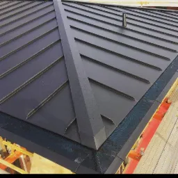 Nowoczesne, grafitowe pokrycie dachowe z metalu, widok z góry na fragment dachu z rynnami zabezpieczonymi siatką w Zgierzu, widoczny kominek wentylacyjny.