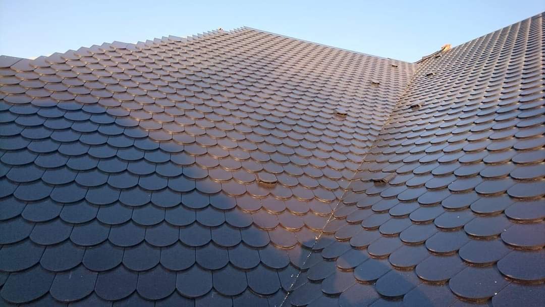 Dach pokryty ciemnymi, okrągłymi płytkami przypominającymi rybią łuskę, widoczne załamania dachu i refleksy światła na powierzchni.