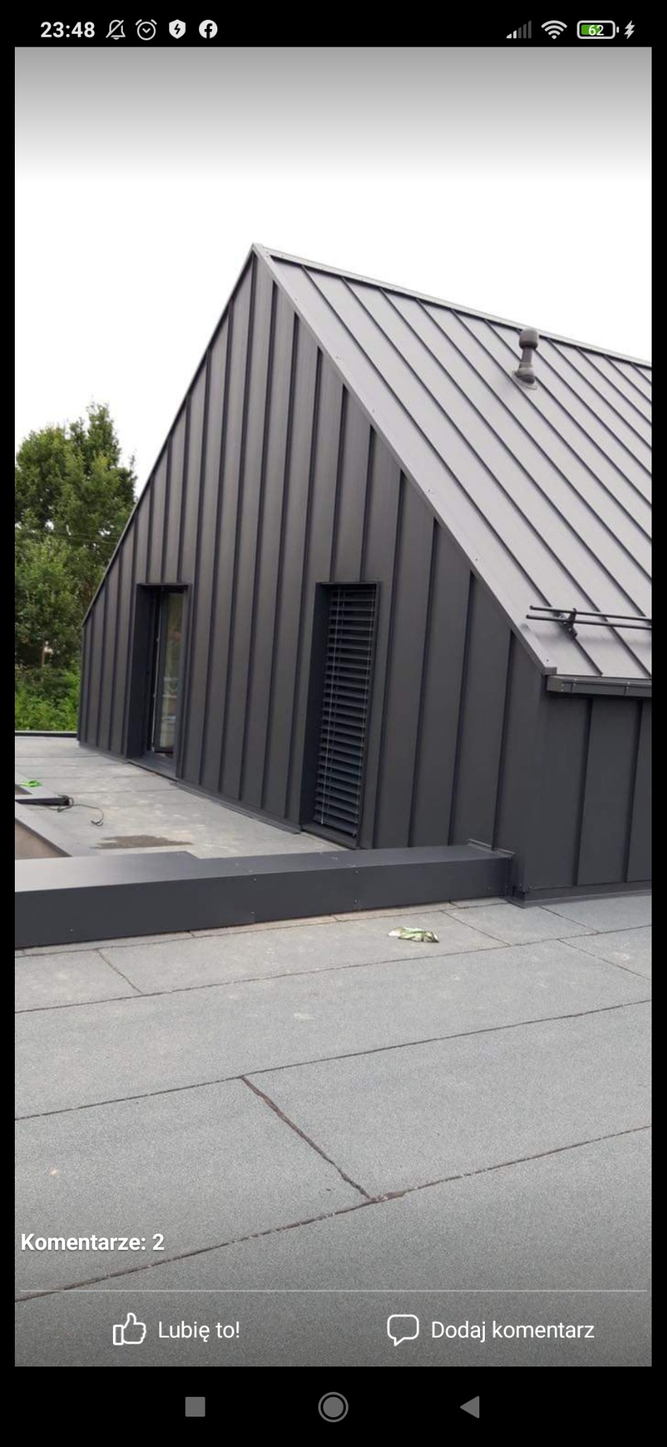 Nowoczesny dom z ciemnoszarą, metalową elewacją i dachem z blachy na rąbek stojący, widok z poziomu dachu, na którym leżą śmieci.