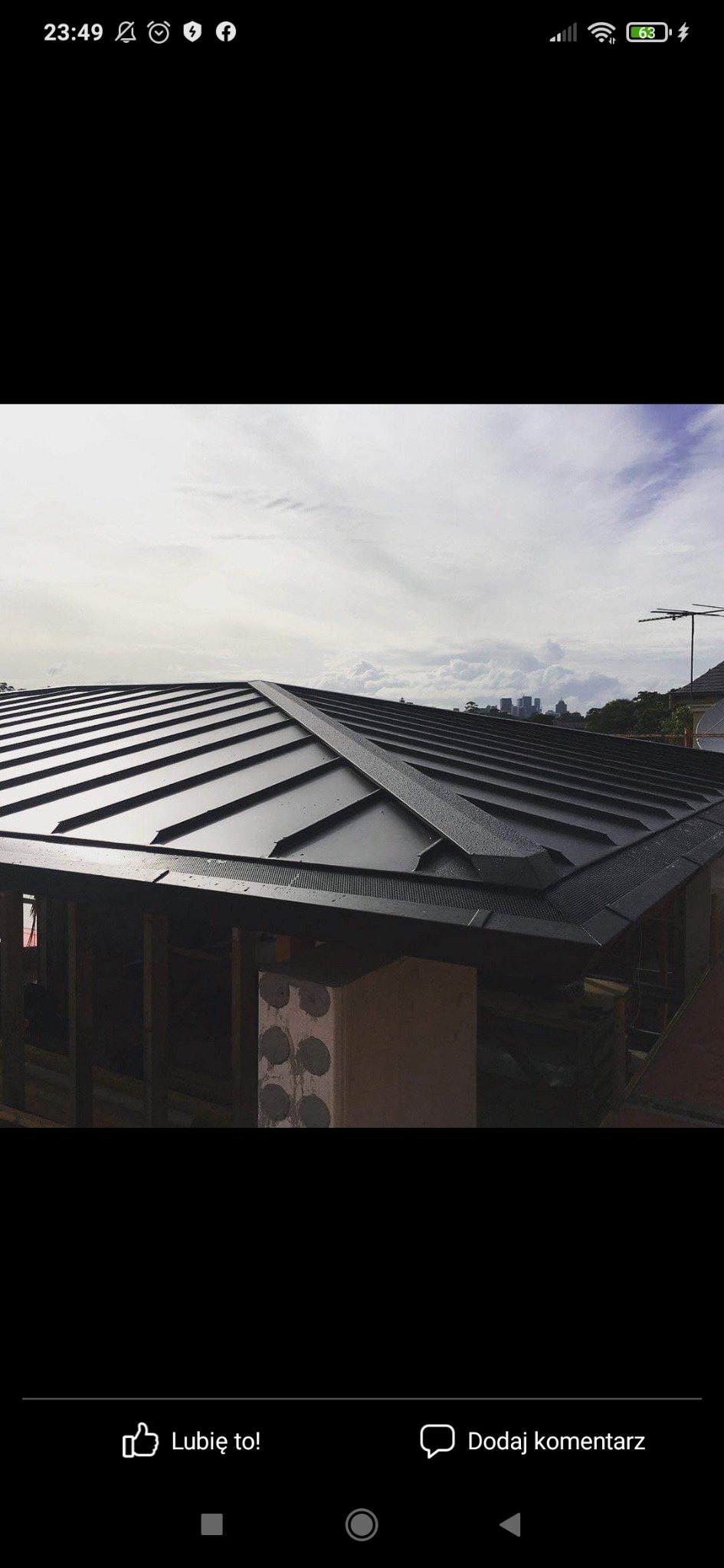 Nowoczesny, czarny dach z blachy na budynku z widocznymi elementami konstrukcyjnymi i fragmentem miasta w tle.