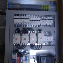 Rozdzielnica elektryczna z bezpiecznikami, stycznikami i przewodami zamontowana w szarej szafie, widoczne oznaczenia K1, K2, K3, K4, Eaton, Schneider, Mean Well, Litex EVO 6000.