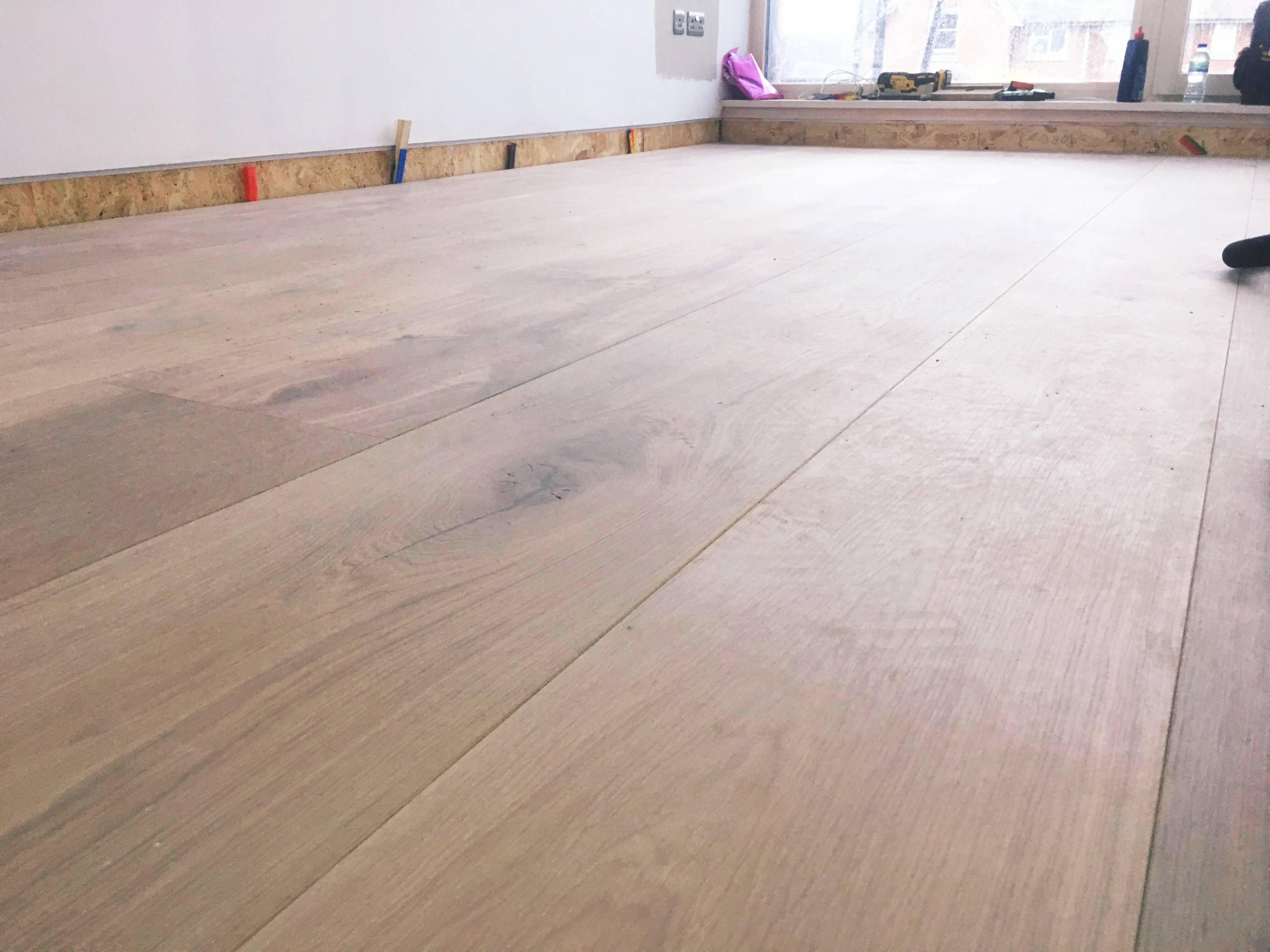 Układanie jasnych paneli podłogowych z widocznym fragmentem okna i narzędziami w tle.