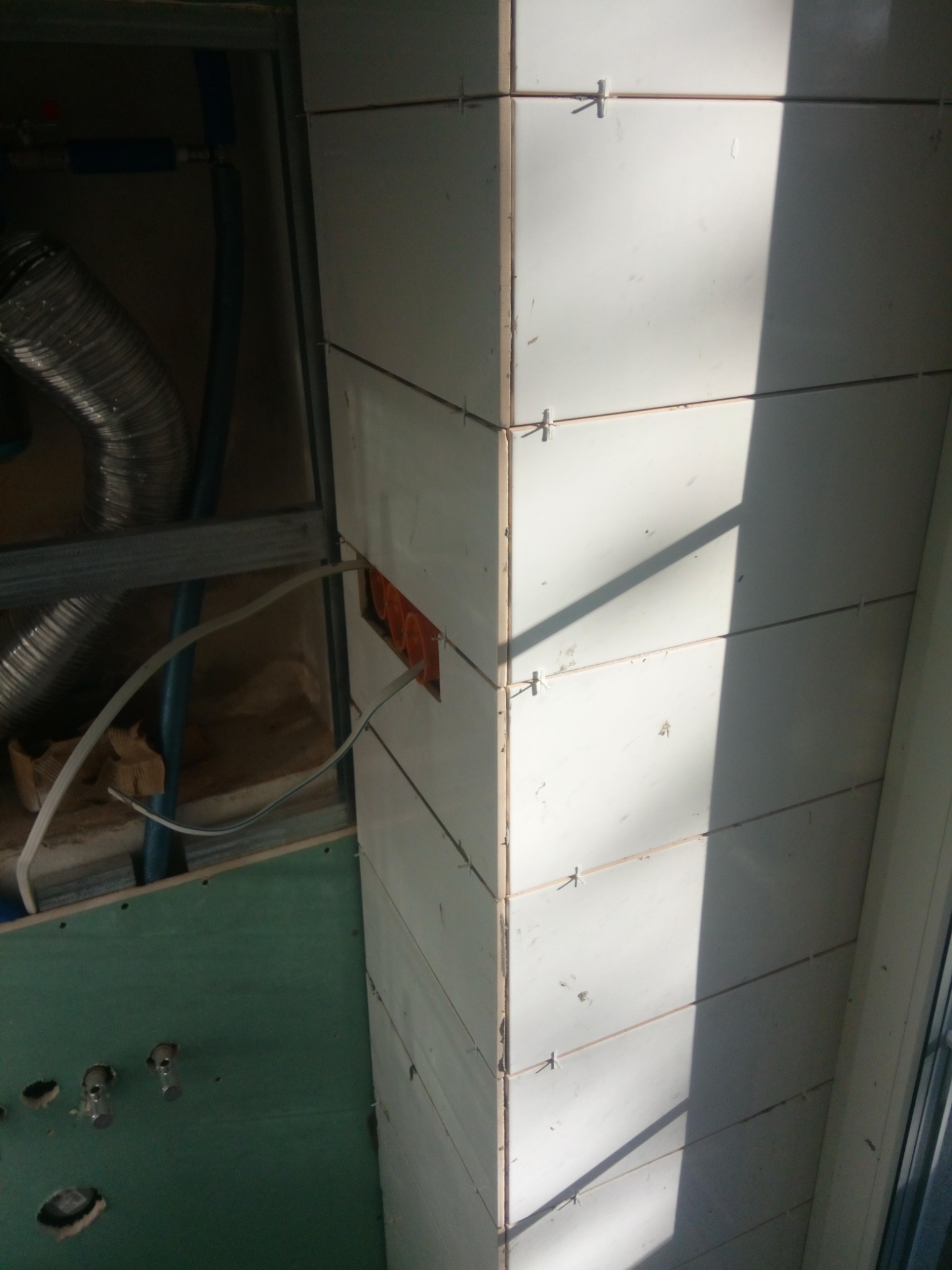 Układanie białych płytek na narożniku w Lublinie, widoczne krzyżyki dystansowe i instalacja elektryczna w tle.