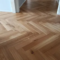 Ułożona podłoga z parkietu w jodełkę, widok z perspektywy korytarza, ściany w trakcie wykończenia.