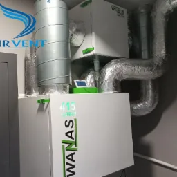 Zainstalowana jednostka wentylacyjna z rekuperacją WanAs 415 Hi-Tech z widocznymi przewodami wentylacyjnymi w izolacji aluminiowej, na ścianie szarej ściany, z wyświetlaczem parametrów pracy.