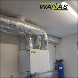 AIR VENT Nowicki Rekuperacje Sp. z o.o. - Zamontowana centrala rekuperacyjna z izolowanymi przewodami wentylacyjnymi w pomieszczeniu. Widoczny filtr wody i gniazdko elektryczne.