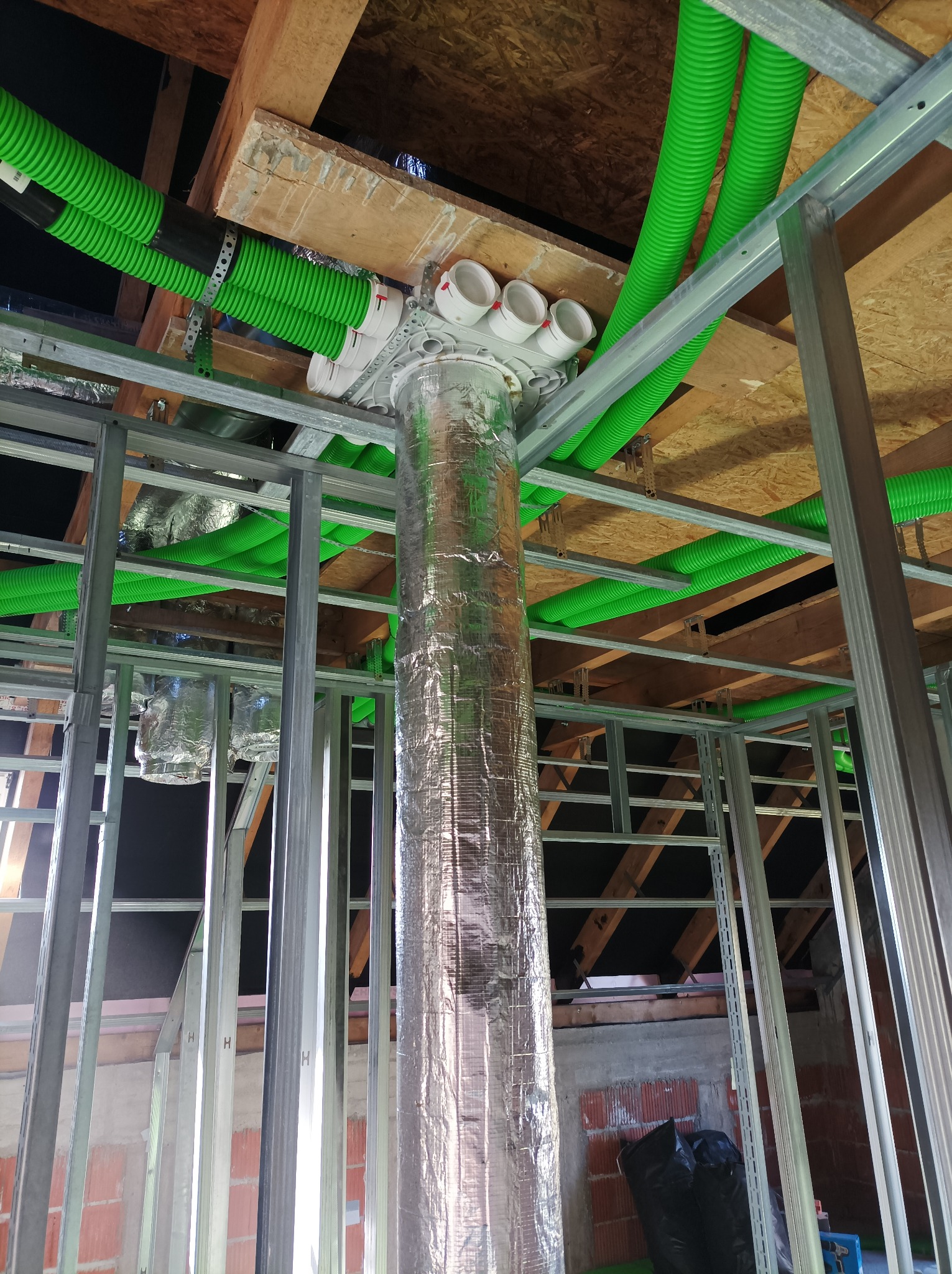 System kanałów wentylacyjnych z rurami w kolorze zielonym, rozchodzącymi się pod stropem, w trakcie montażu w surowym budynku z metalową konstrukcją szkieletową ścian działowych.