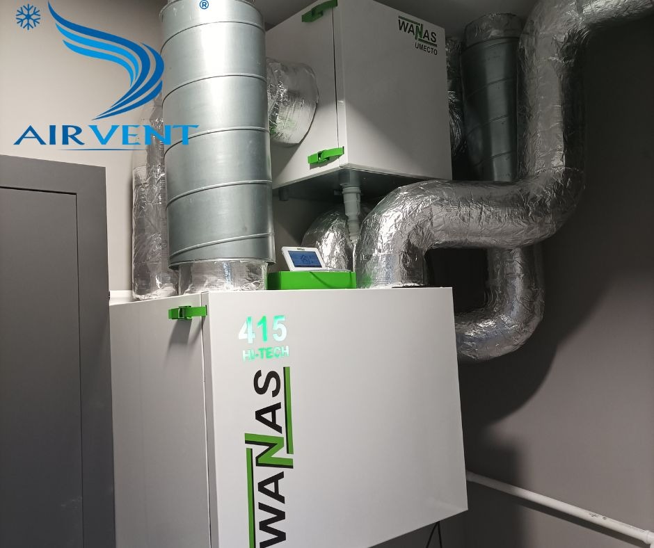 Zainstalowana jednostka wentylacyjna z rekuperacją WanAs 415 Hi-Tech z widocznymi przewodami wentylacyjnymi w izolacji aluminiowej, na ścianie szarej ściany, z wyświetlaczem parametrów pracy.