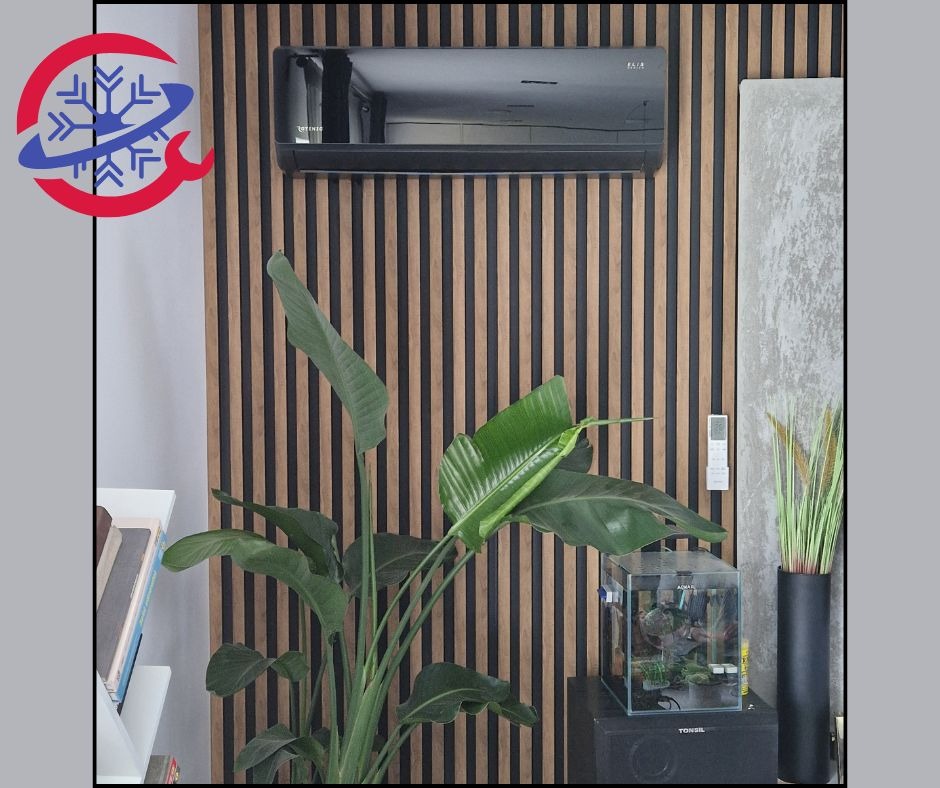 Czarna jednostka klimatyzacyjna na ścianie z drewnianych paneli, z rośliną strelicji i akwarium w pomieszczeniu.