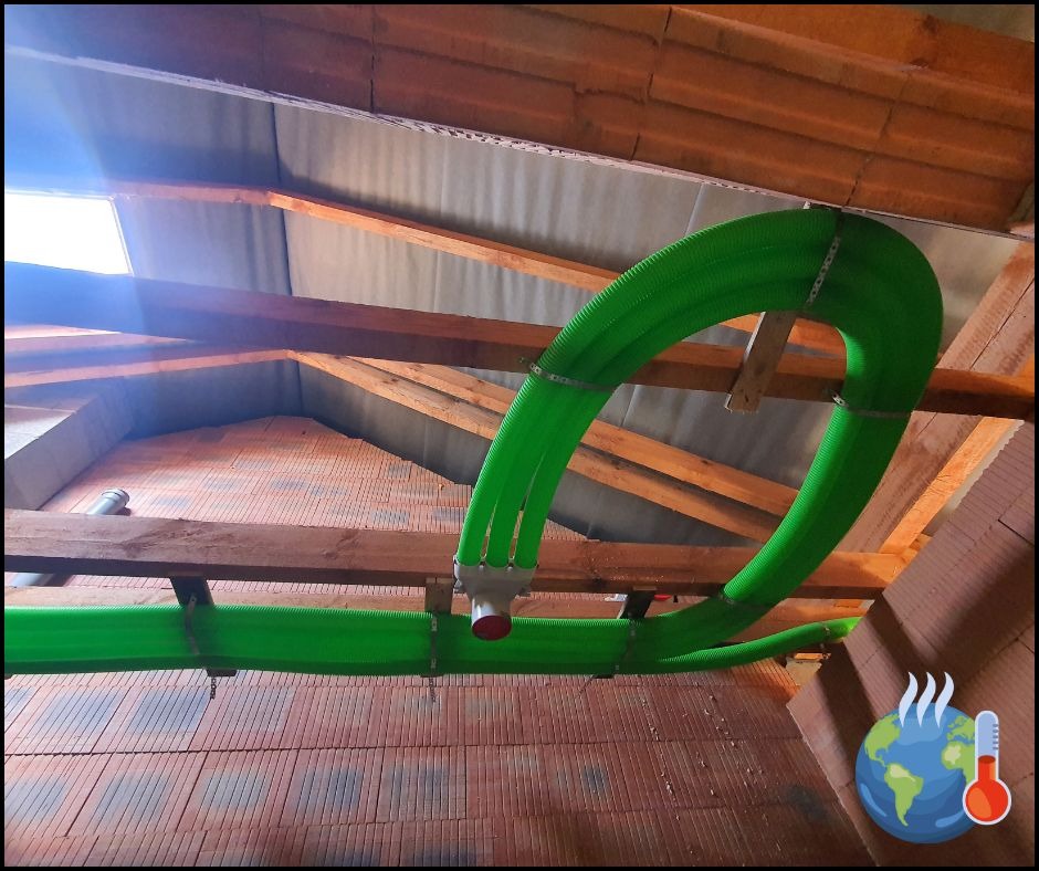 Zielone rury wentylacyjne zamontowane pod drewnianą konstrukcją dachu z widocznym oknem dachowym. Instalacja w surowym stanie, przed wykończeniem.