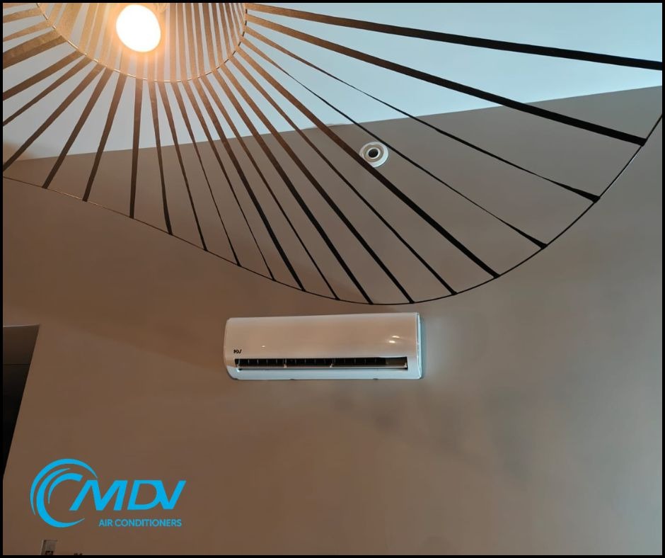 Biały klimatyzator na ścianie pod dekoracyjnym oświetleniem sufitowym z czarnymi pasami. Widoczny czujnik. Minimalistyczny design wnętrza.