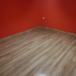 Fragment pokoju z nową podłogą z paneli laminowanych o jasnym odcieniu drewna, ściany pomalowane na intensywny czerwony kolor.