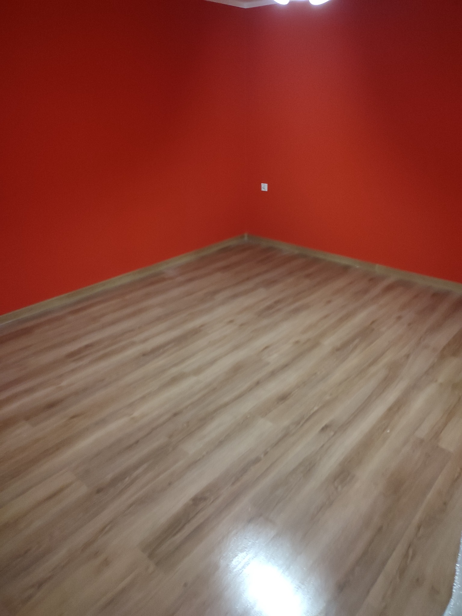 Fragment pokoju z nową podłogą z paneli laminowanych o jasnym odcieniu drewna, ściany pomalowane na intensywny czerwony kolor.