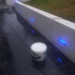 Onyx - Świeżo pomalowany murem z wbudowanymi niebieskimi lampami LED, obok stoi wiadro z farbą, mokra, czarna posadzka.