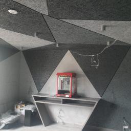 Onyx - Pokój z akustyczną okładziną ścian i sufitu w geometryczne wzory, szaro-biała kolorystyka, oświetlenie punktowe, czerwony automat do popcornu na półce, widoczne kable i sprzęt elektroniczny.