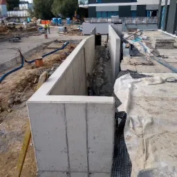 Betonowy wykop fundamentowy z widoczną izolacją pionową w postaci membrany kubełkowej, na placu budowy nowego budynku.