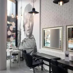 Wnętrze salonu kosmetycznego we Wrocławiu z białymi ceglanymi ścianami, czarnymi fotelami fryzjerskimi i dużym plakatem kobiety na ścianie.