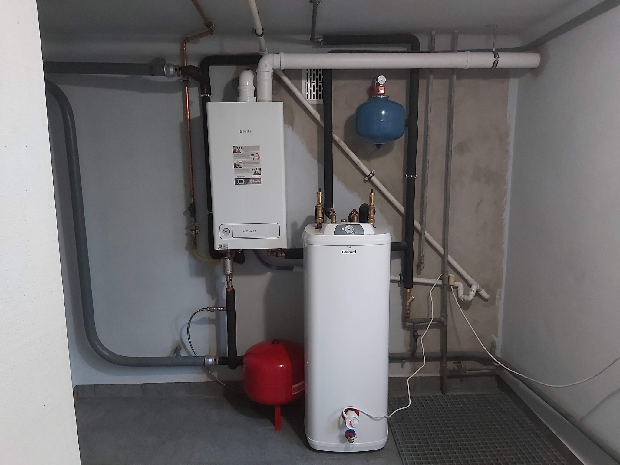 Instalacja kotła gazowego Beretta z zasobnikiem Galmet i widocznymi rurami instalacji grzewczej oraz zbiornikami wyrównawczymi w kotłowni.