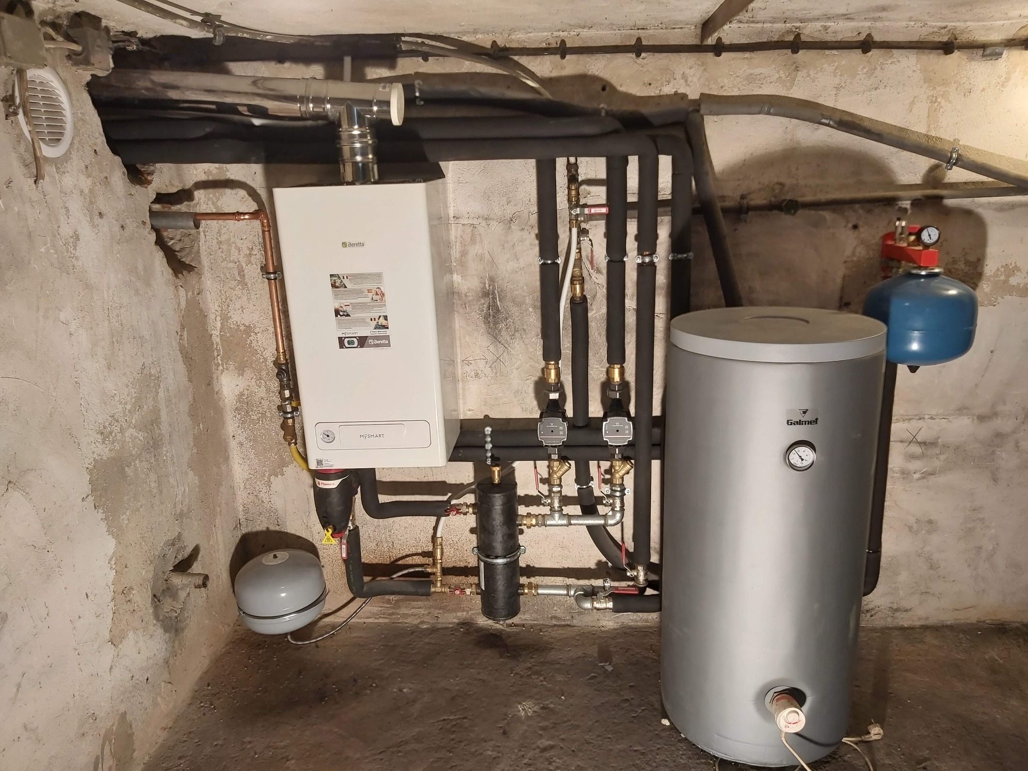 Kocioł gazowy Beretta, zbiornik akumulacyjny Galmet i instalacja hydrauliczna w piwnicy z surowymi ścianami.