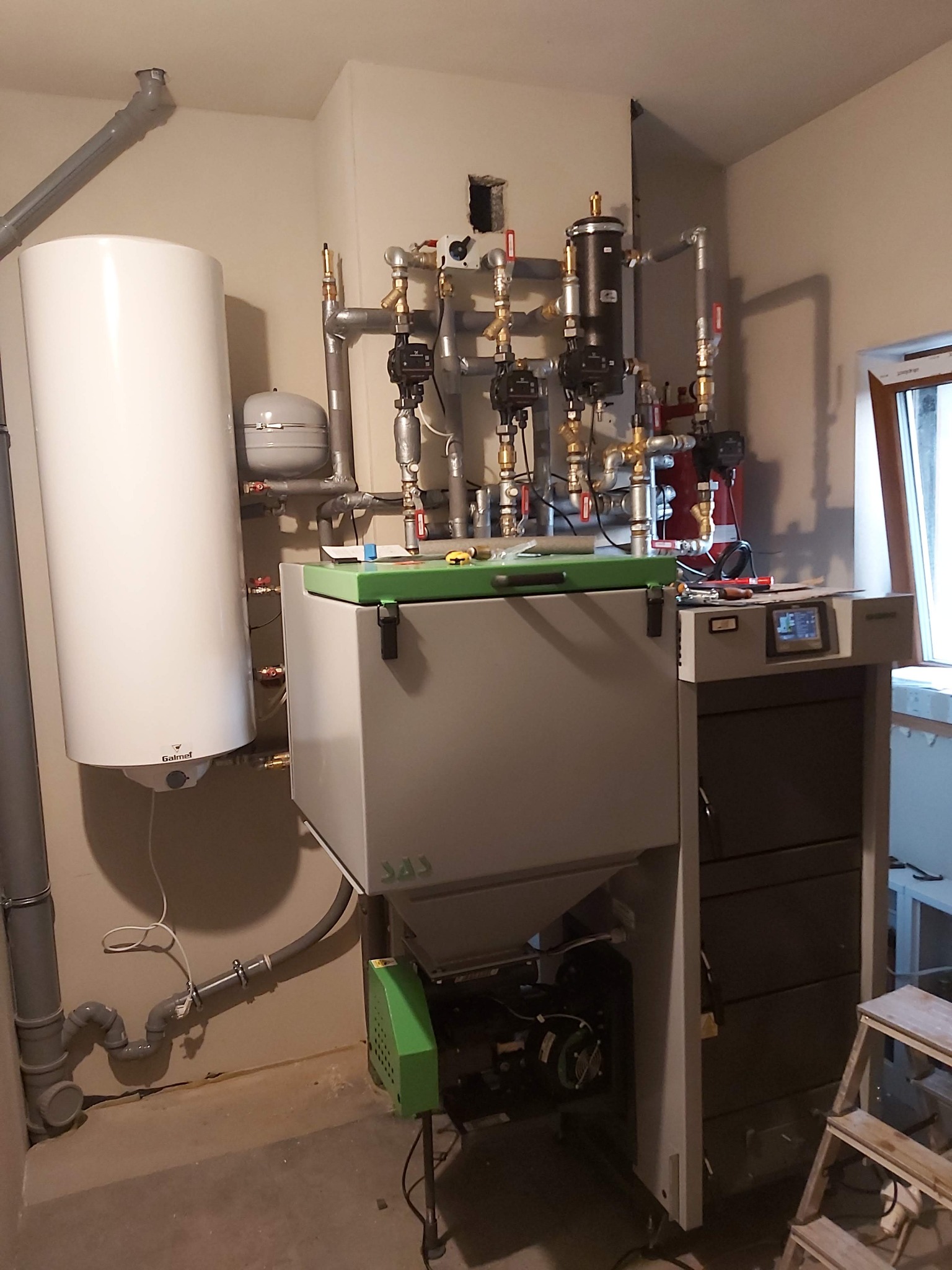 Kotłownia z zamontowanym kotłem na paliwo stałe SAS, zasobnikiem Galmet i osprzętem hydraulicznym, widoczne rury, zawory i sterownik elektroniczny