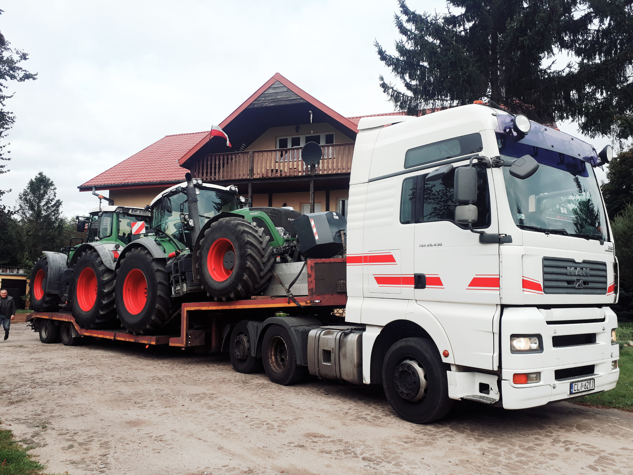 Laweta z dwoma traktorami marki Fendt na tle domu z polską flagą w Lipnie.