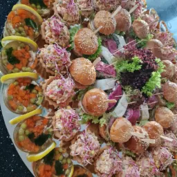 Dekoracyjna taca z przekąskami: galaretki warzywne z cytryną, tartaletki z pastą i kiełkami, mini burgery z sezamem oraz roladki z warzywami i sałatą.