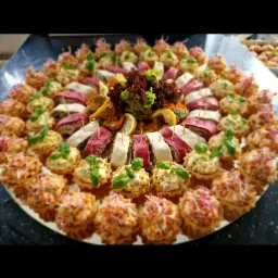 Dekoracyjnie ułożone na talerzu mini tartaletki z sałatką, roladki z szynki i tortilli, ozdobione zieleniną i cytryną.