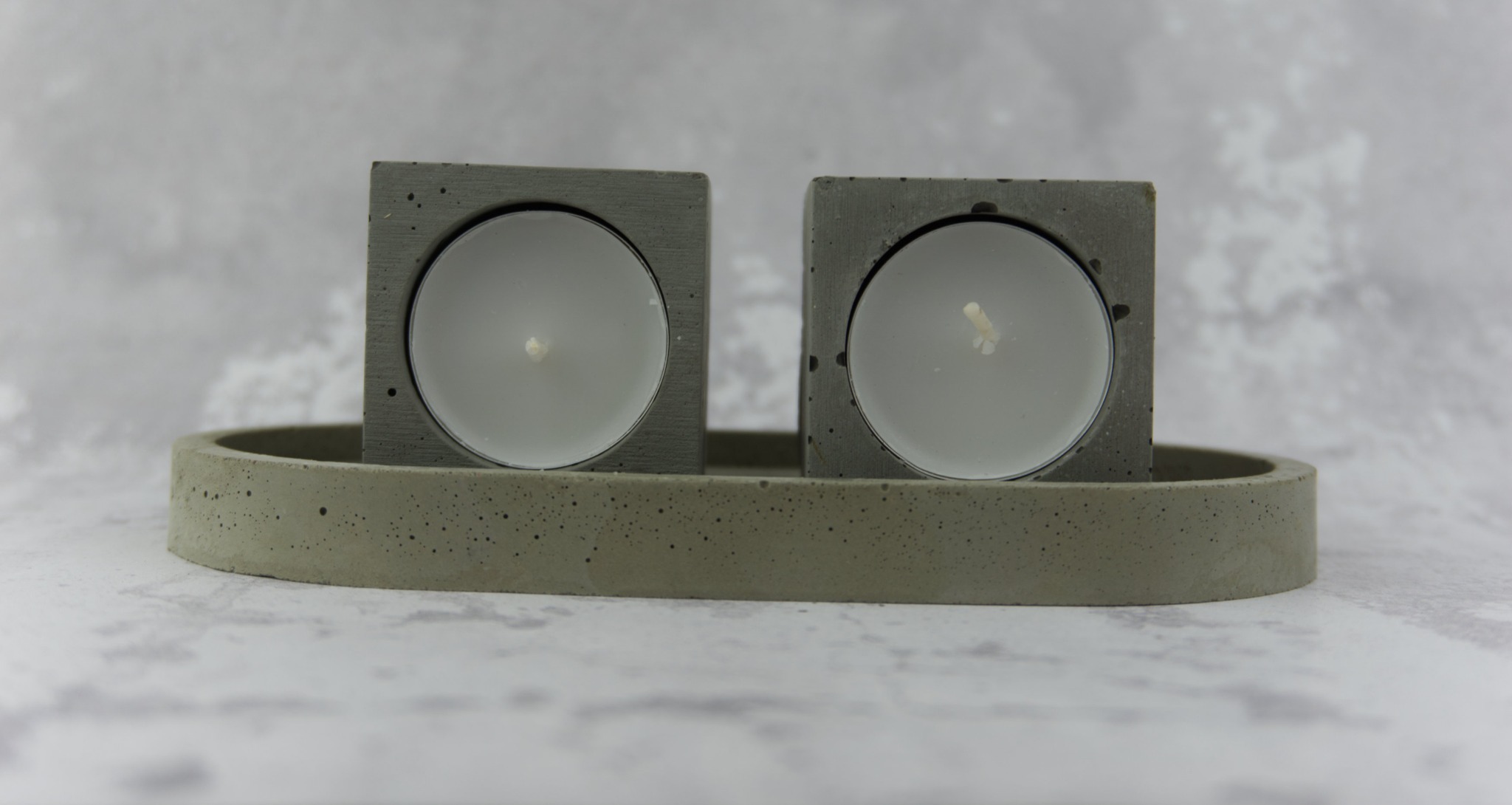 Dekoracyjny, betonowy świecznik na dwie tealighty, o surowej fakturze, na tle marmurowej płyty.