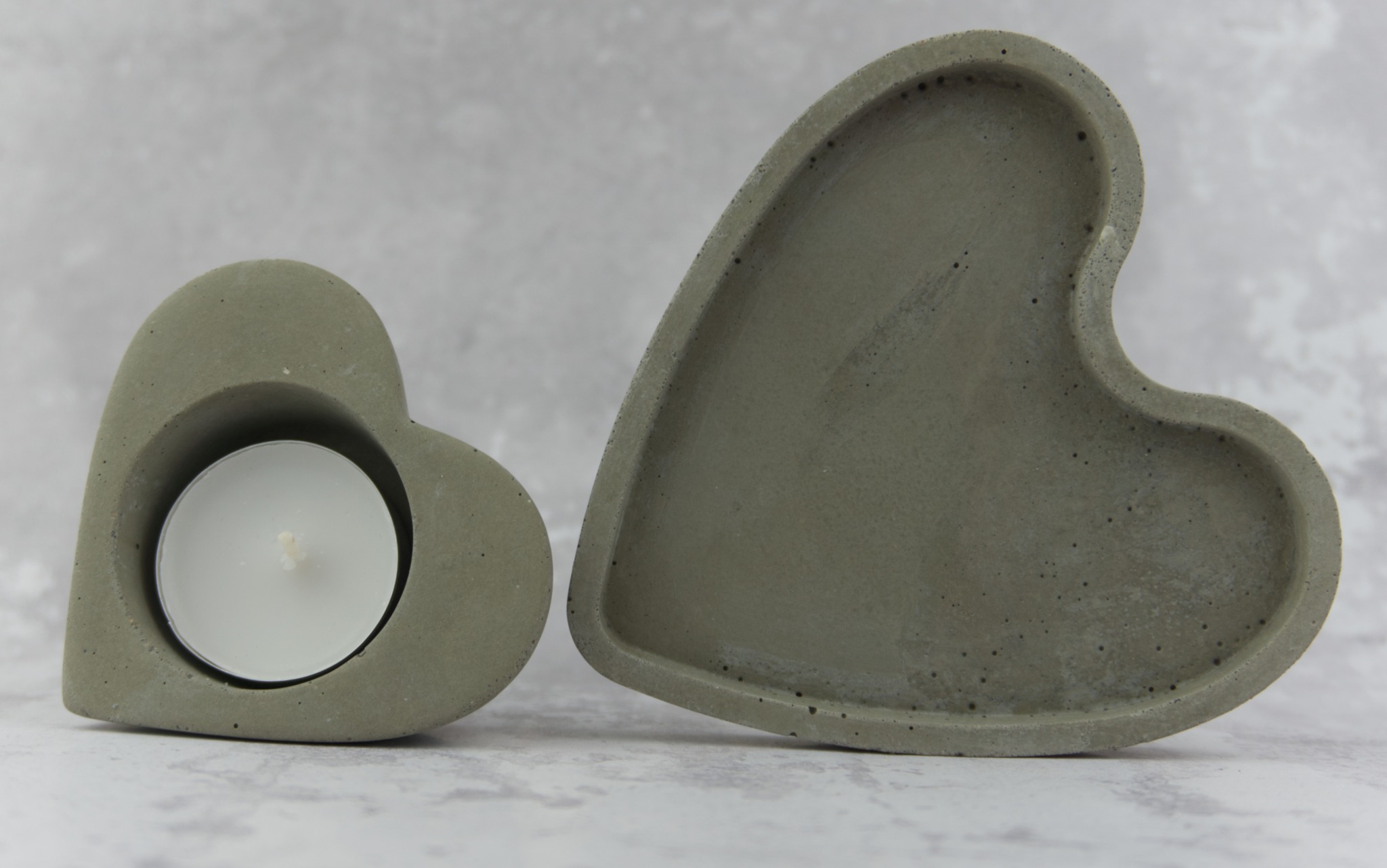 Dwa betonowe serca: jeden jako świecznik z białą tealight, drugi jako patera, na tle marmurkowym.